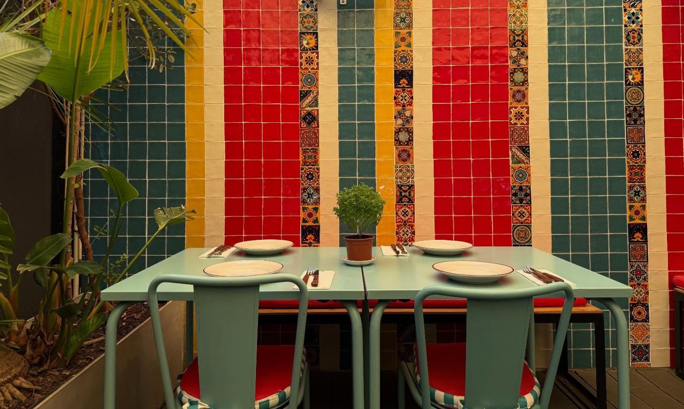 Sala do Stella com parede de azulejos em riscas vermelhas, amarelas e verdes e mesas verde-água