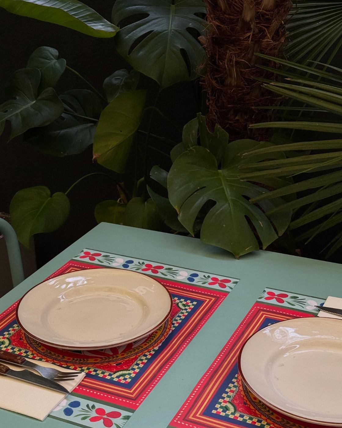Mesa posta com toalhas bordadas entre plantas
